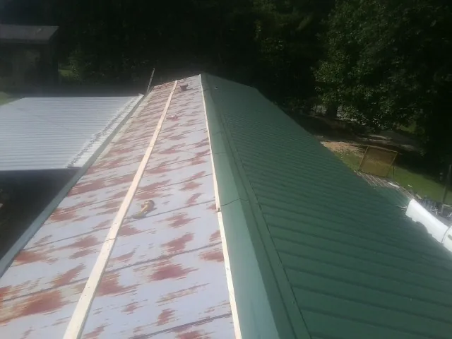 Old rusted panels beside newly installed green metal roofing — Wind Damage Roof Repair by Roofing Brothers in Advance