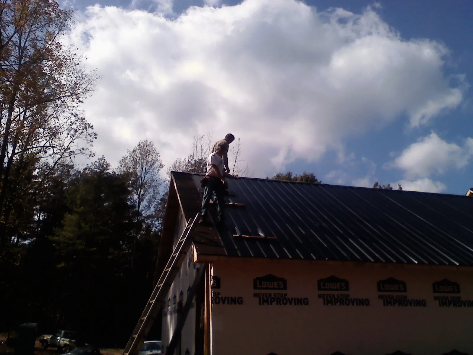 Roofer fastening dark metal panels high against a cloudy sky, from a Roof Inspection job in Advance